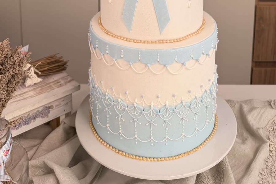 Base del pastel con guardas en glasé, volados celestes y ribete de perlas doradas